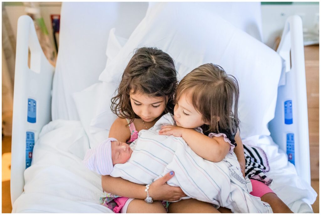 Newton Wellesley Hospital two big sisters hold newborn baby on hospital bed photo