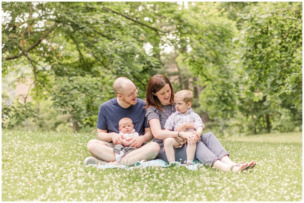 family with newborn sits on blanket in field for family photo
