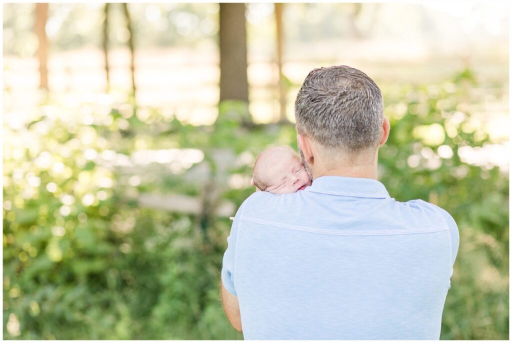 dad hold baby on shoulder for outdoor newborn photo session
