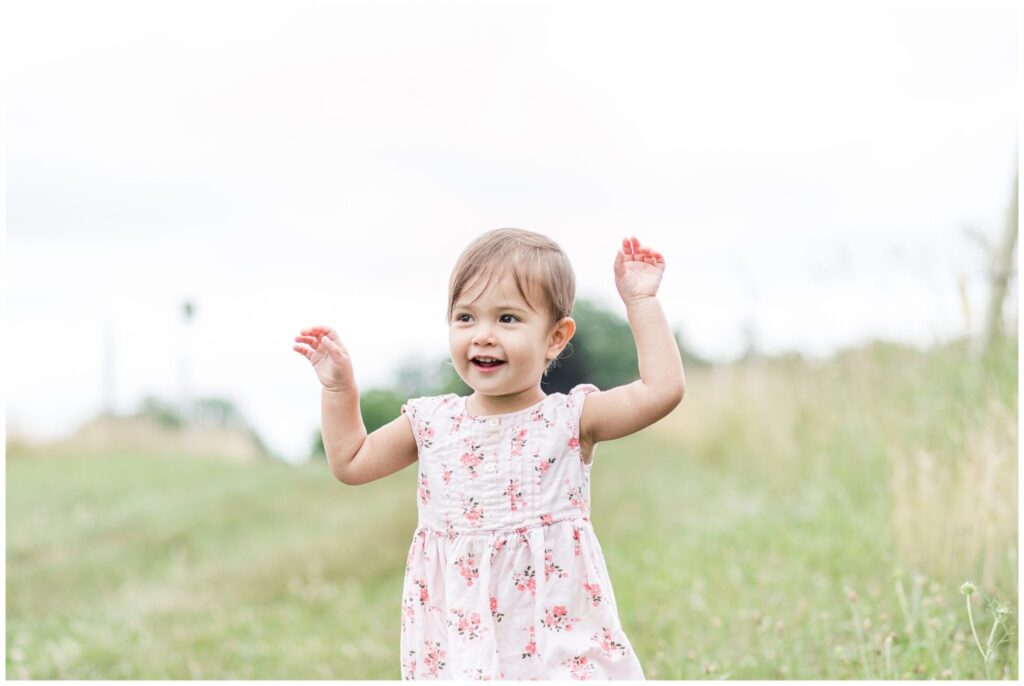 toddler runs in field with arms up