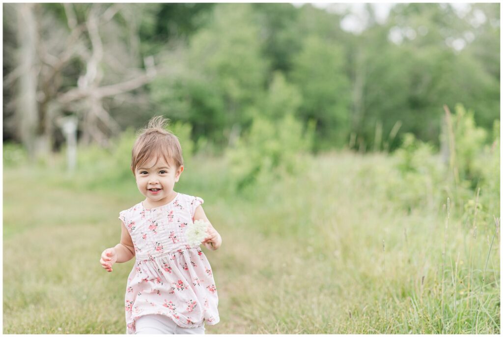 little girl in field holding flower runs toward camera for photo
