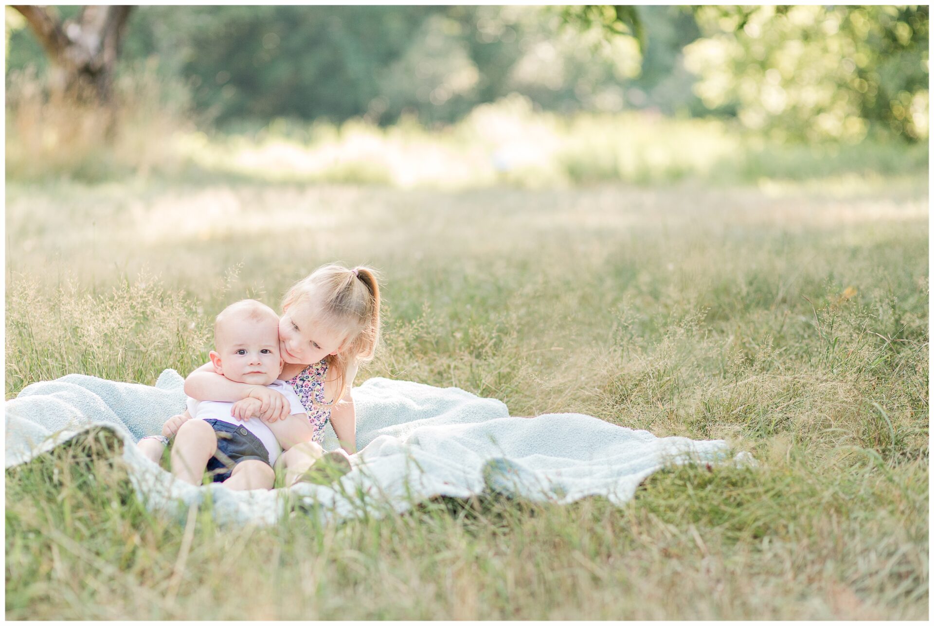 sister holds baby brother on blanket for family photo session in Sherborn Massachusetts