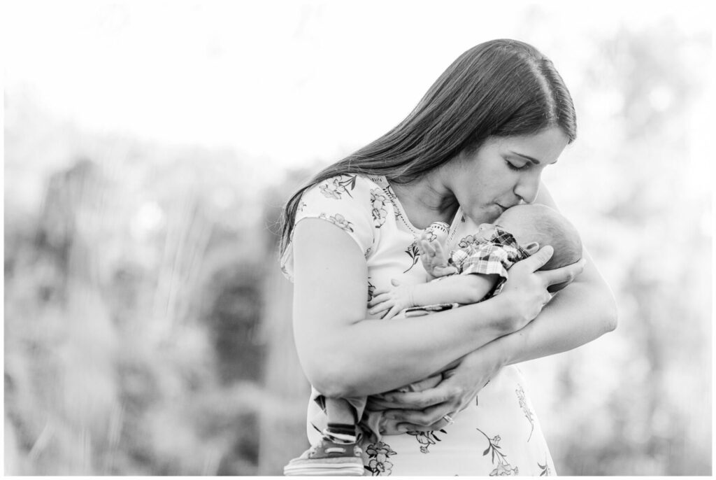black and white photo of mom kissing newborn during outdoor photo session metro west Boston Massachusetts