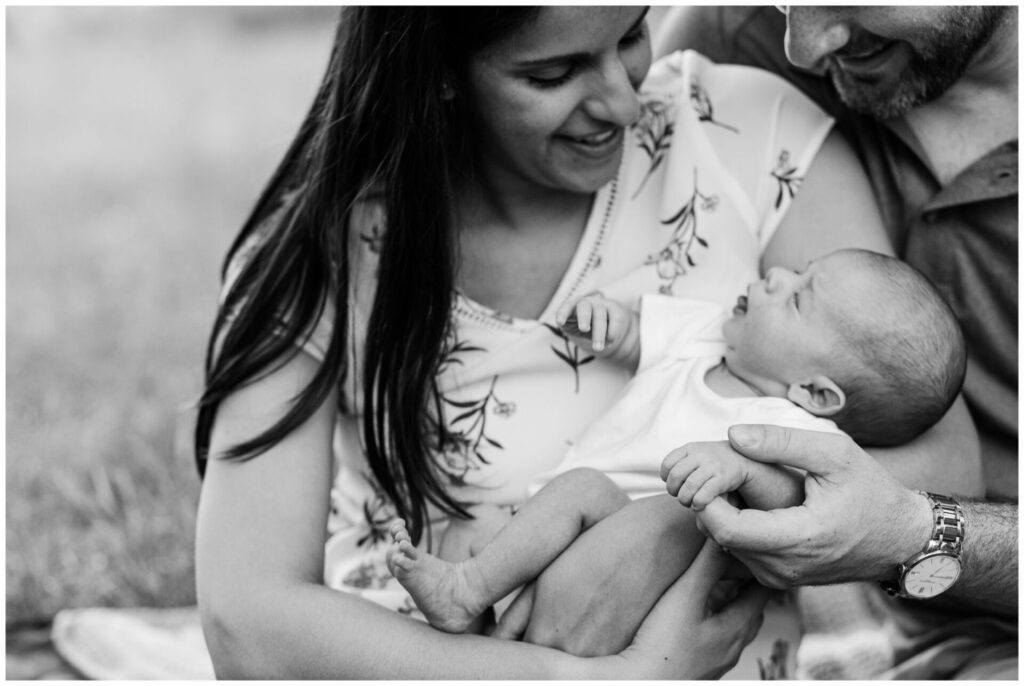 black and white photo of parents holding newborn baby while baby holds dads finger in Massachusetts