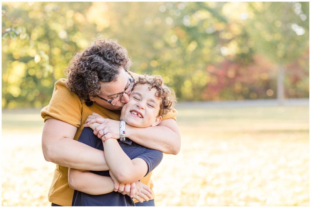 mom kisses sons cheek for family photo session at Elm Bank Reservation Wellesley Massachusetts