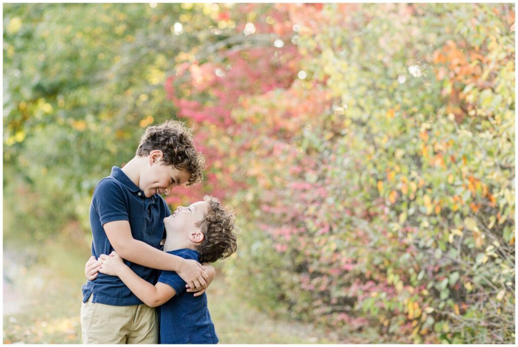 brother smile at each other while hugging for family photo Wellesley Massachusetts 