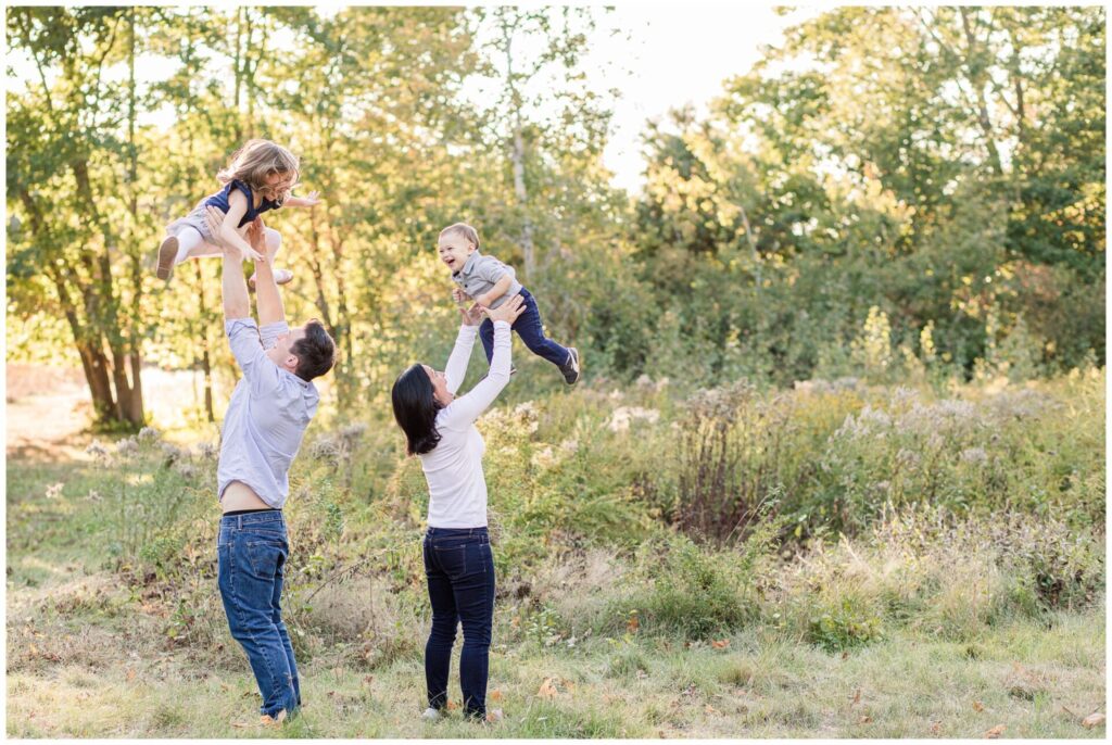 parents throw son and daughter in the air for family photo in field in Wayland Massachusetts