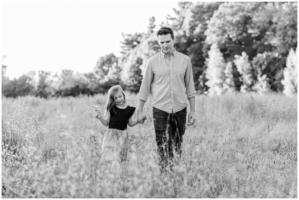 black and white photo of father and daughter holding hands walking through field in Wayland Massachusetts
