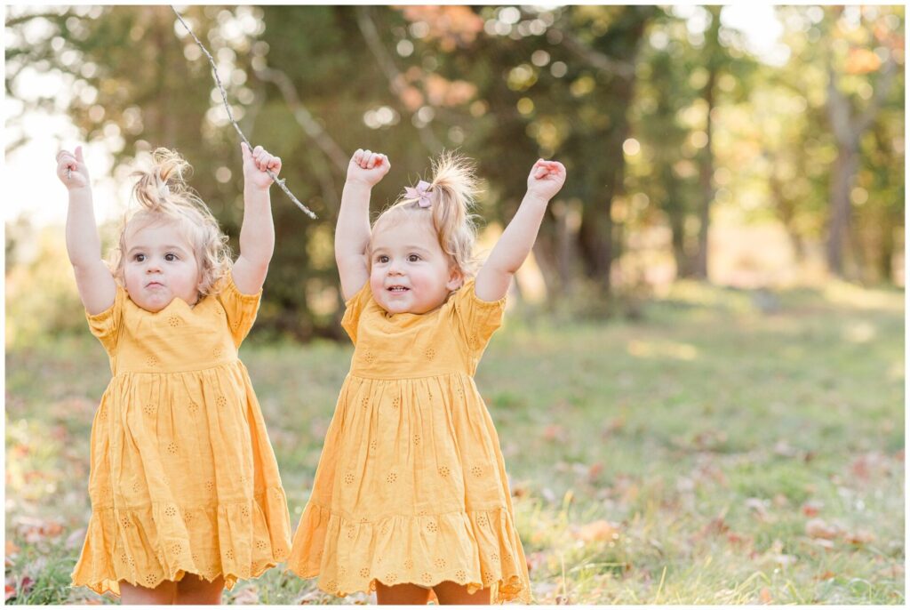 Twin toddlers raise arms in the air sining if your happy and you know it for family photos in Wayland Massachusetts