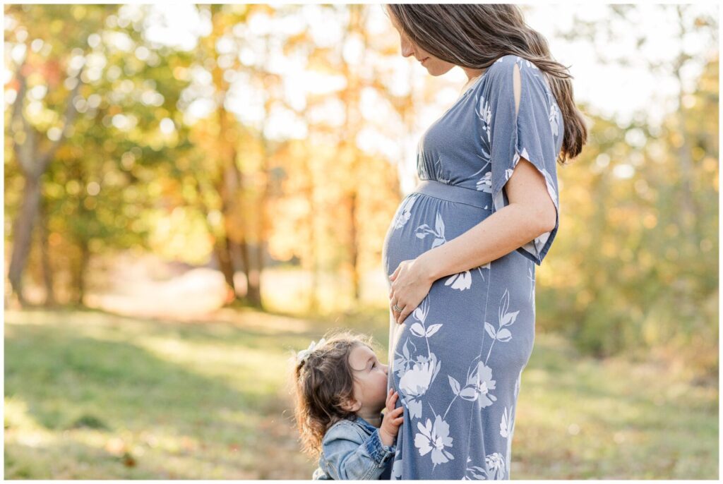 Toddler girl kisses mom's belly for maternity photo session Natick Massachusetts