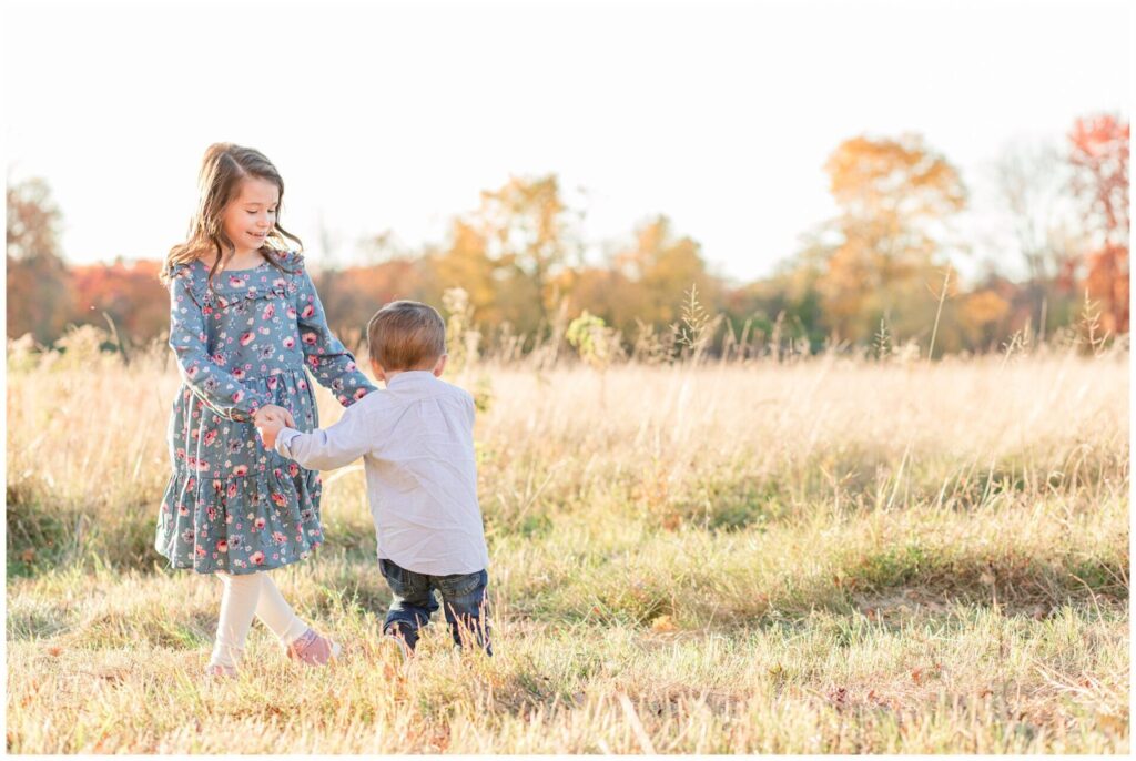 brother and sister play in field holding hands for family photo session Natick Massachusetts