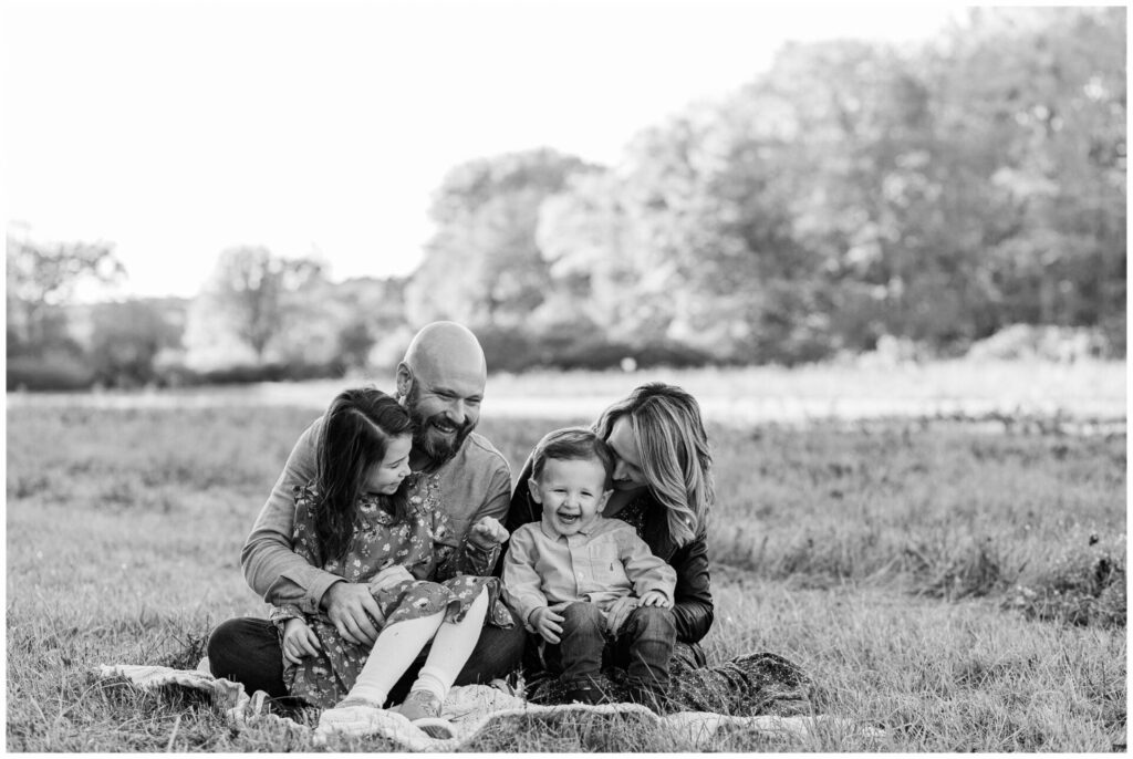 Natick Massachusetts family laughs together on a blanket in field for soon to be mom of 3 Maternity family photo session