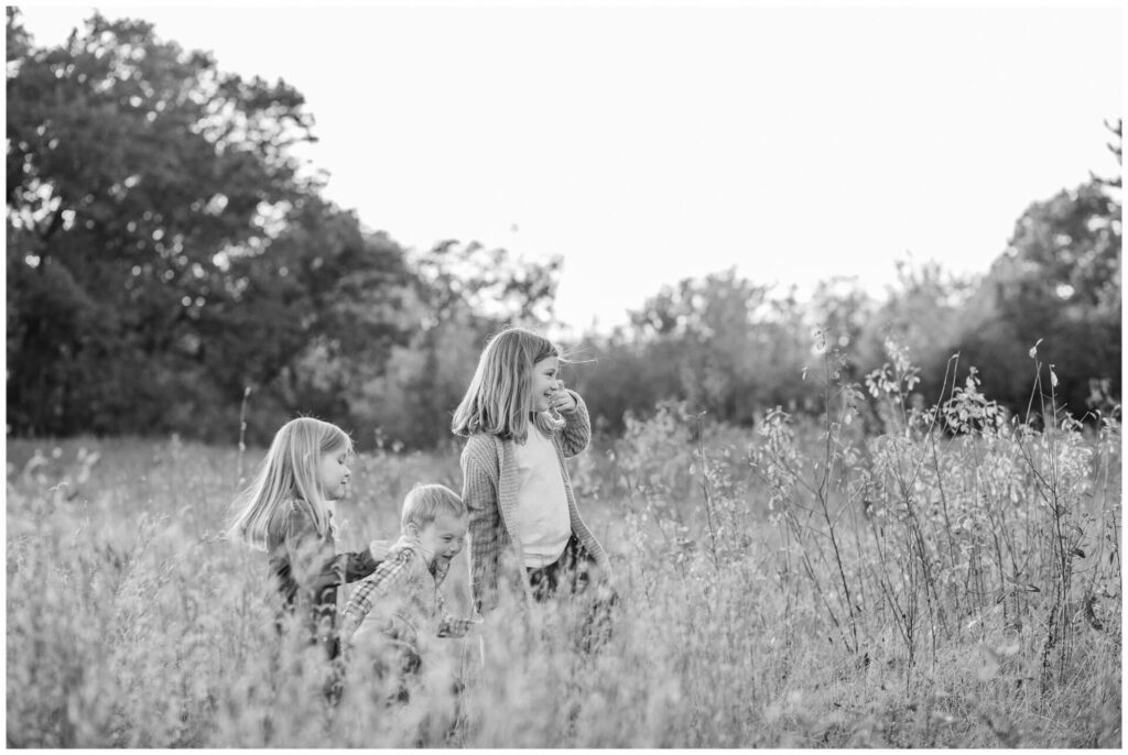 Black and white photo of siblings walking through field Wayland Massachusetts