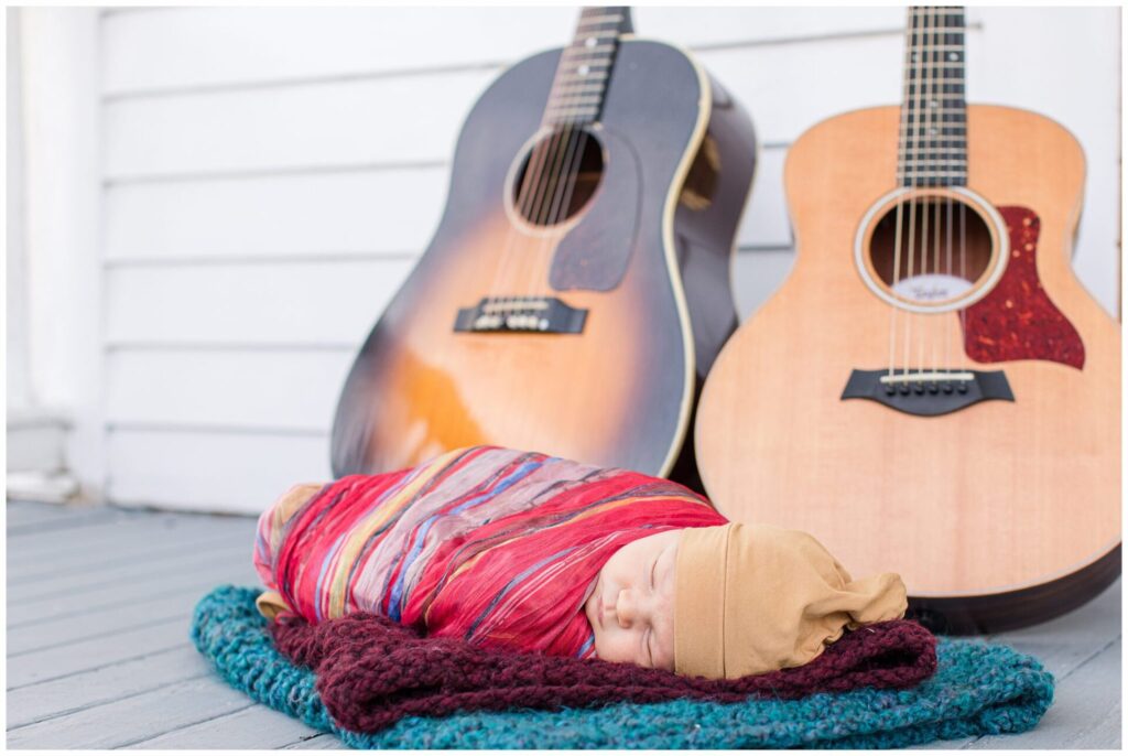 Baby sleeps on blankets in front of guitars during outdoor newborn photo session