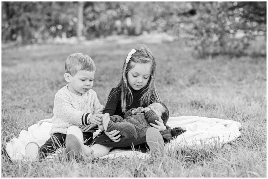 Black and white photo of brother and sister holding newborn baby brother at Dowses Orchard Sherborn MA