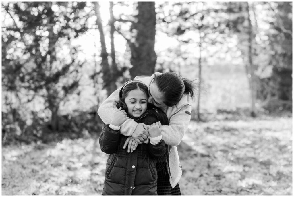 black and white photo of mom kissing daughter on the cheek during winter photo session in Wayland Massachusetts