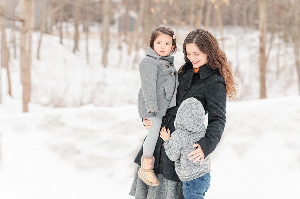 Mom standing in the snow smiles at her children during family photo session in Natick Massachusetts for NICU blog