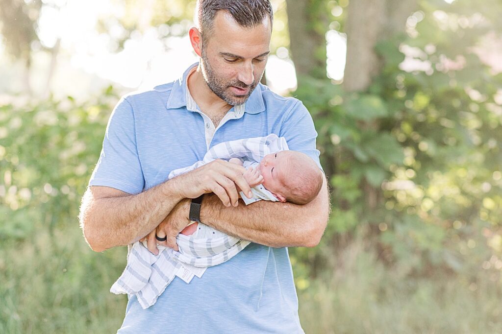 newborn holds fathers finger during outdoor newborn photo session at Barber Reservation, Sherborn Massachusetts
