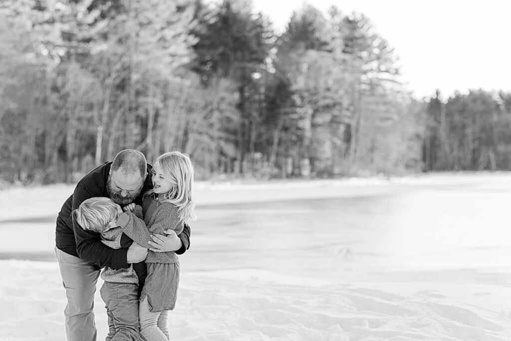 Black and white photo of father hugging children in front of Wayside Inn Grist Mill pond, Sudbury MA