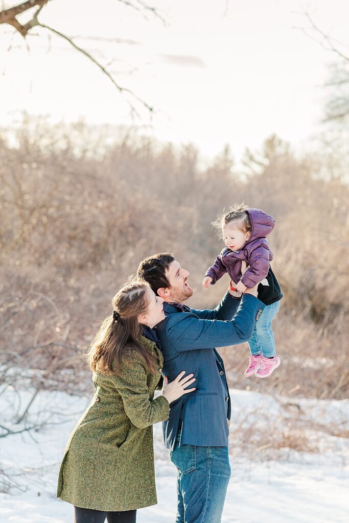Parents smile at daughter while dad holds daughter up high during family photo session for NICU experience blog at Barber Reservation, Sherborn Massachusetts