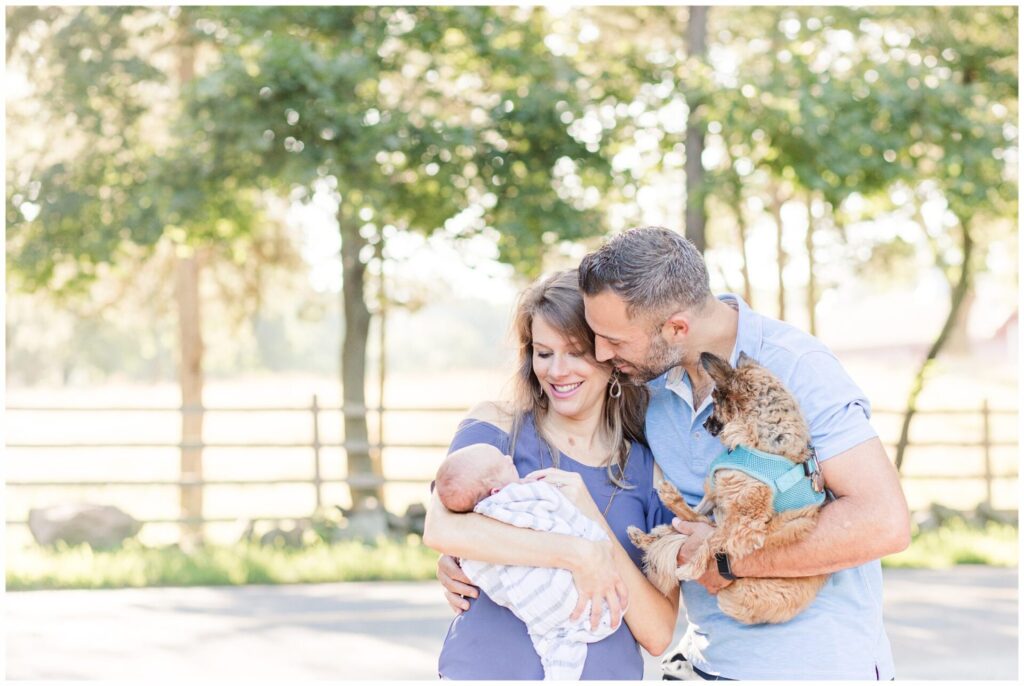 Parents hold baby and dog during outdoor newborn photo session at Barber Reservation, Sherborn Massachusetts