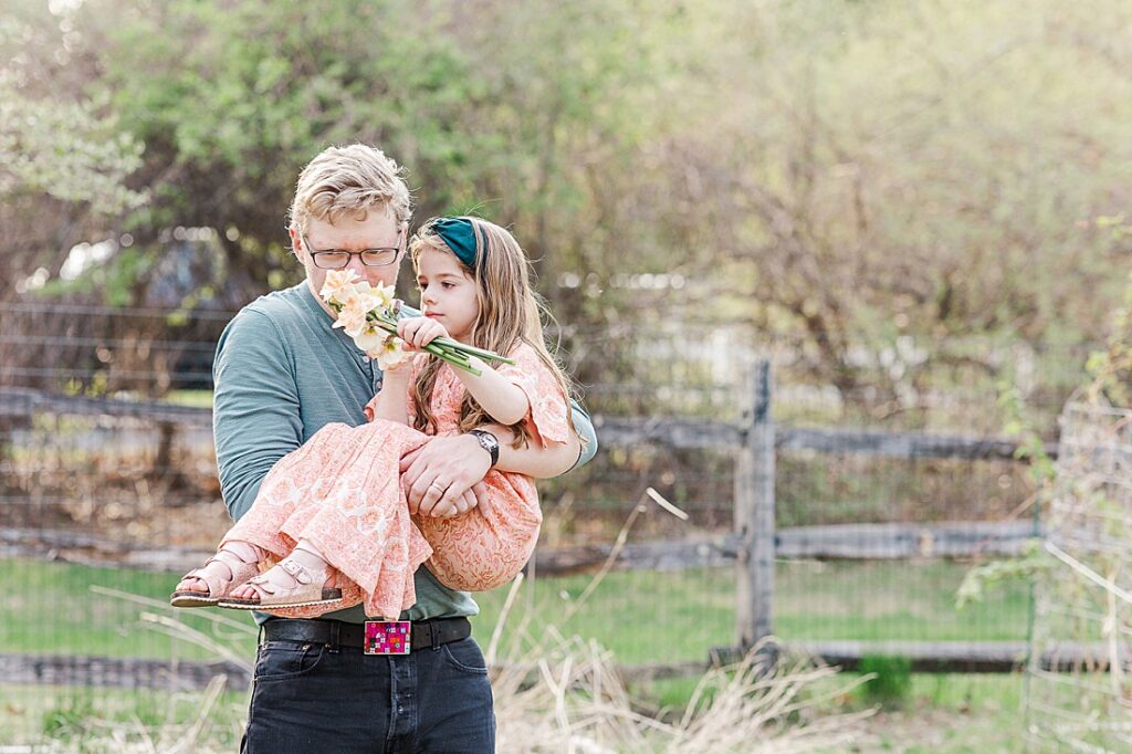 father holds daughter and smells flowers she picked during family photo session with Sara Sniderman Photography in Sherborn Massachusetts