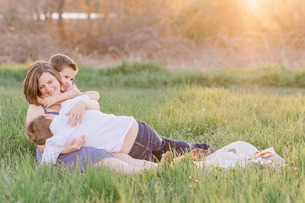 Mom cuddles on blanket in a field during family photo session with Sara Sniderman Photography at Heard Farm, Wayland Massachusetts