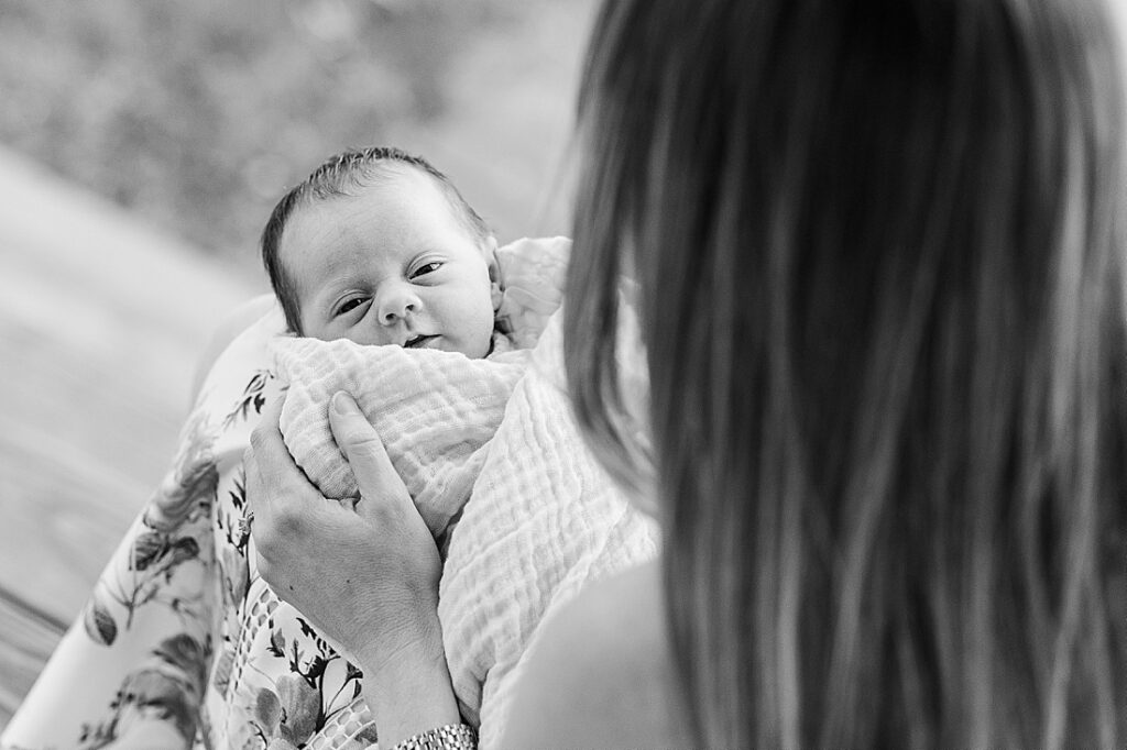 black and white photo of newborn on moms lap on porch during back yard newborn photo session in Natick Massachusetts with Sara Sniderman Photography. 