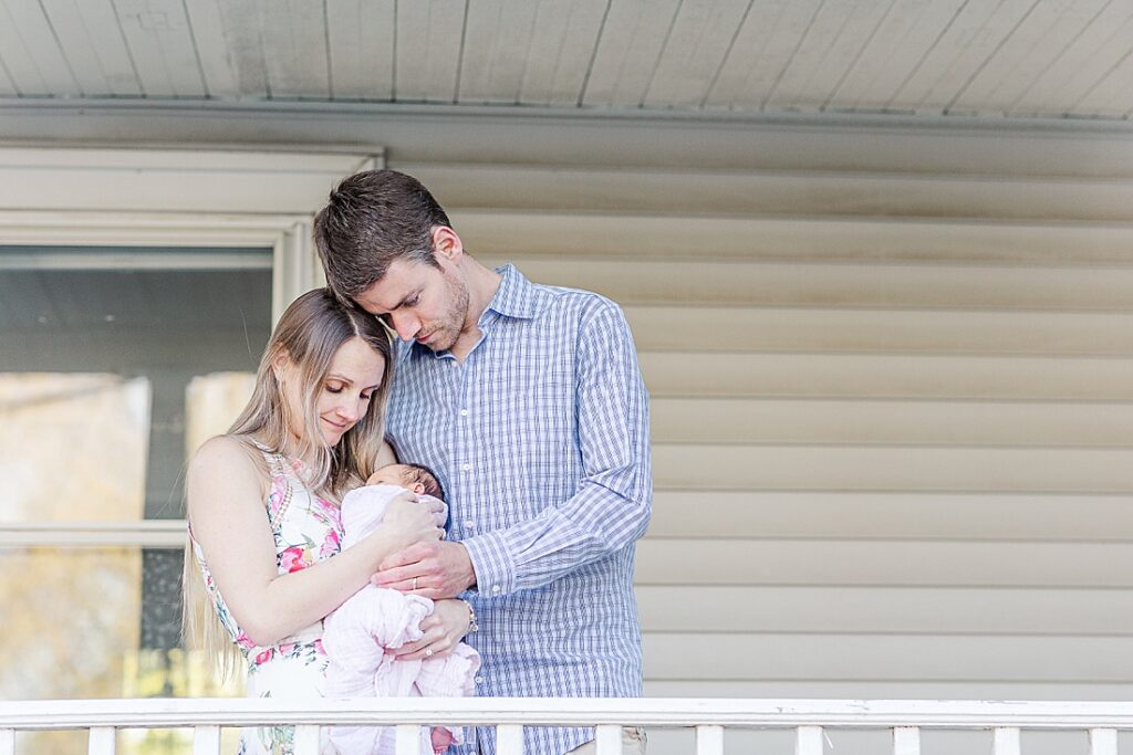 Parents hold newborn on porch during outdoor newborn photo session in Natick Massachusetts with Sara Sniderman Photography. 