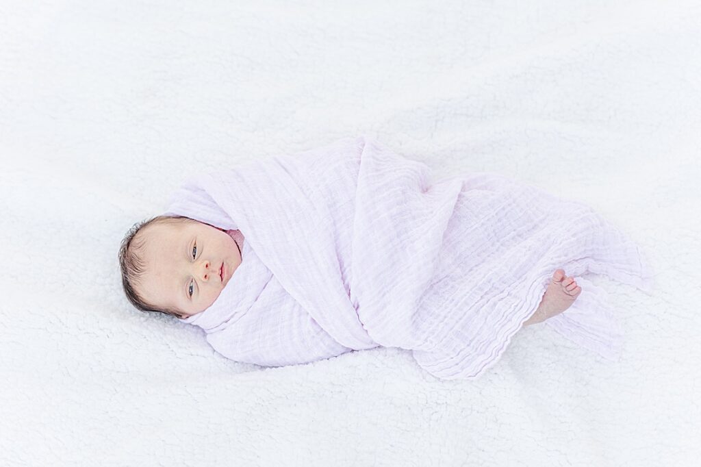 Bay lays on blanket wrapped in blush swaddle during outdoor newborn photo session in Natick Massachusetts with Sara Sniderman Photography. 