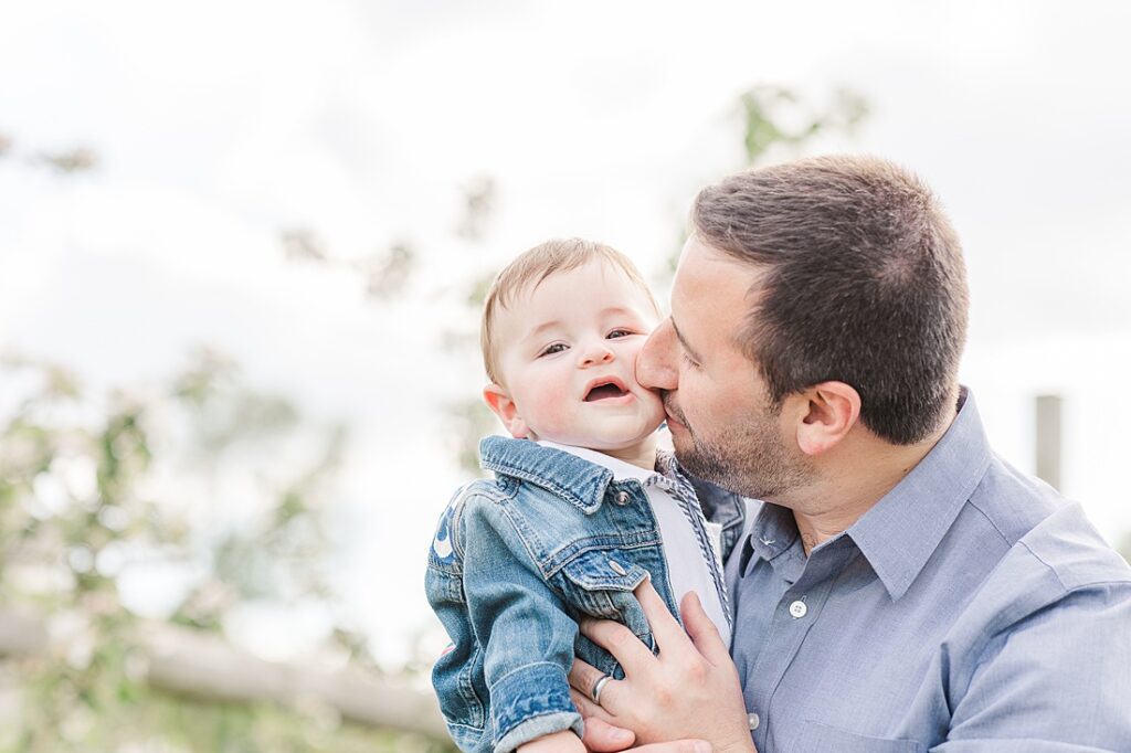 father kisses baby son during family photo session with Sara Sniderman Photography for NICU experience blog at Dowse Orchard, Sherborn Massachusetts