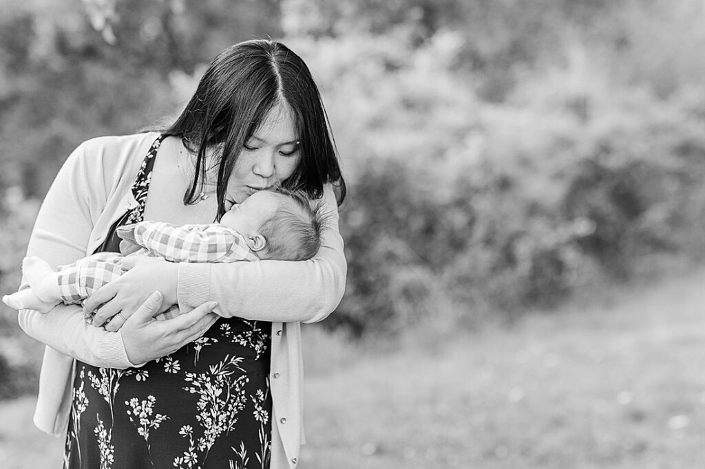 black and white photo of mother kissing newborn during outdoor newborn photo session in Wayland Massachusetts with Sara Sniderman Photography. 