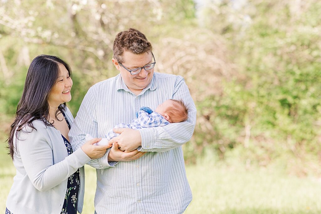 Parents smile at newborn during outdoor newborn photo session in Wayland Massachusetts with Sara Sniderman Photography. 