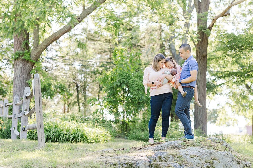 Family stands on rock together during outdoor newborn photo session with Sara Sniderman Photography at Barber Reservation, Sherborn Massachusetts. 