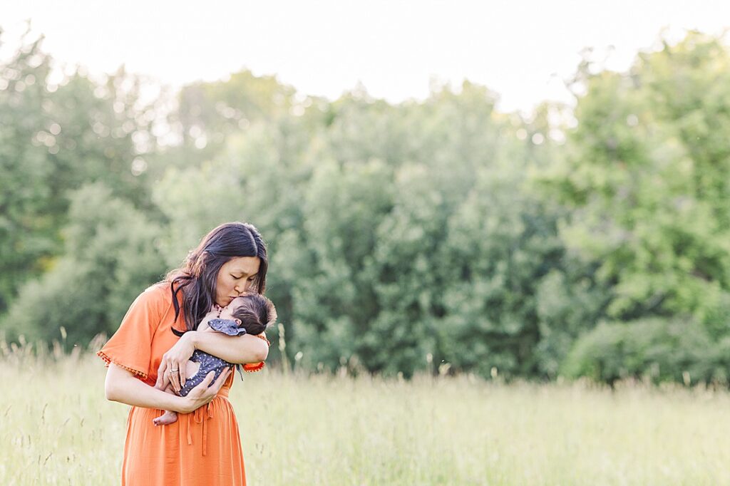 Mom standing in field of tall grass kisses baby on the head during outdoor newborn photo session with Sara Sniderman Photography at Heard Farm, Wayland Massachusetts