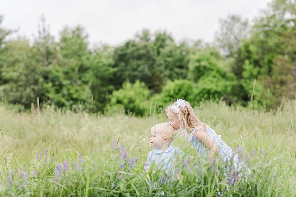 girl kisses toddler brothers head in field of wild flowers during full family photo session with Sara Sniderman Photography at Oak Grove Park, Millis Massachusetts