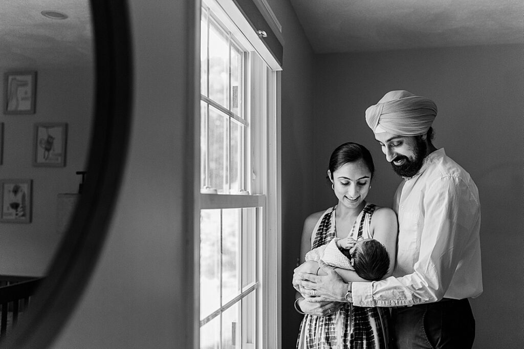 black and white photo of parents holding newborn while standing next to window in nursery during in home newborn photo session with Sara Sniderman Photography in Holliston Massachusetts