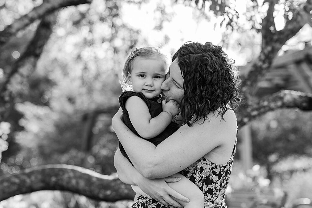 Black and white photo of mom kissing toddler daughter's cheek during extended family photo session with Sara Sniderman Photography at Oak Grove Park, Millis Massachusetts