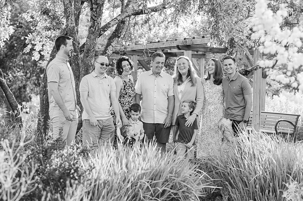 Black and white photo of extended family smiling together in garden during extended family photo session with Sara Sniderman Photography at Oak Grove Park, Millis Massachusetts