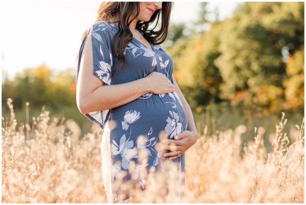 pregnant woman looks down at belly in field of tall grass during maternity photo session with Sara Sniderman Photography at Greenway Conservation Land, Wayland Massachusetts