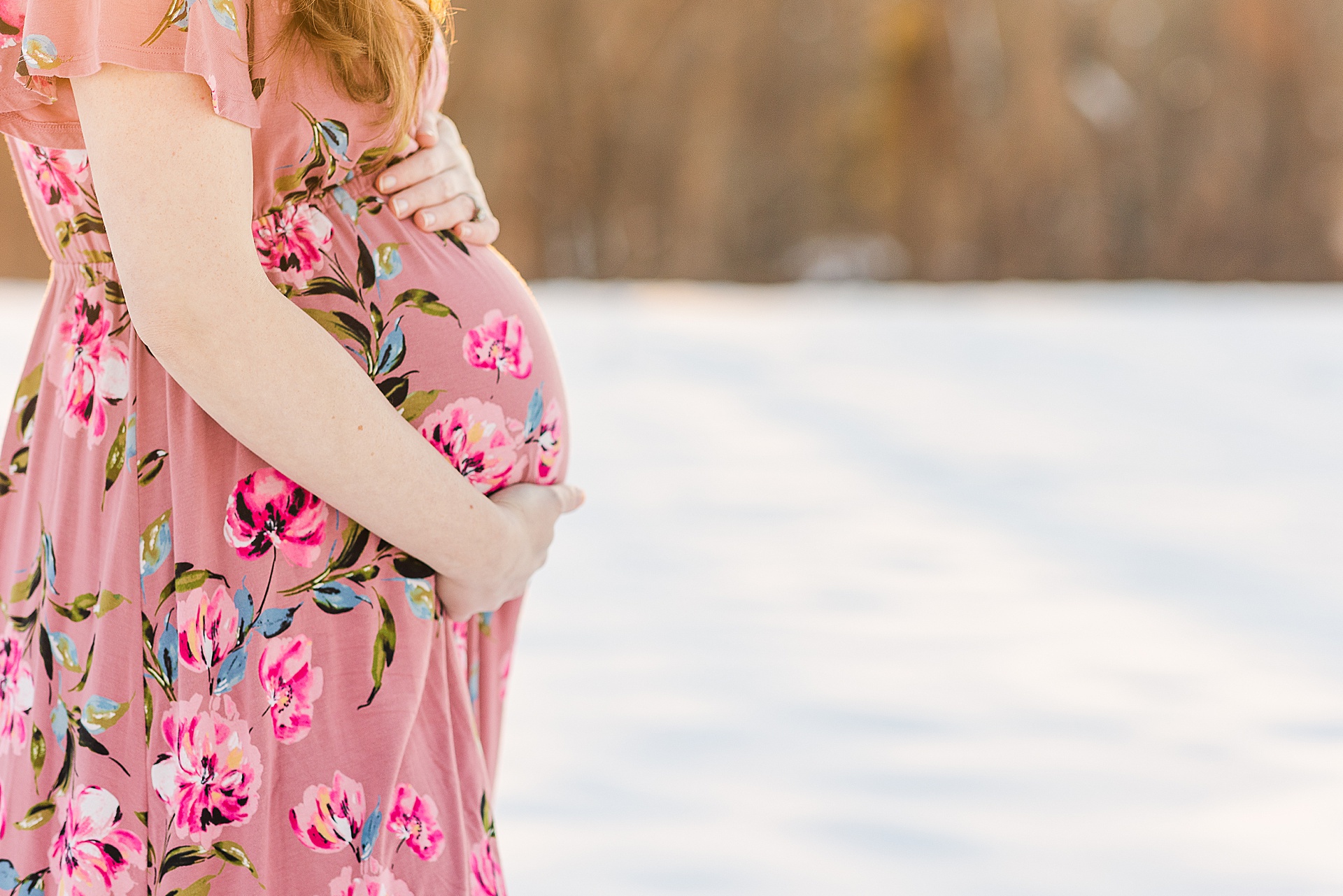 Pregnant woman holds belly during snowy maternity session with Sara Sniderman Photography at Medfield State Hospital Grounds