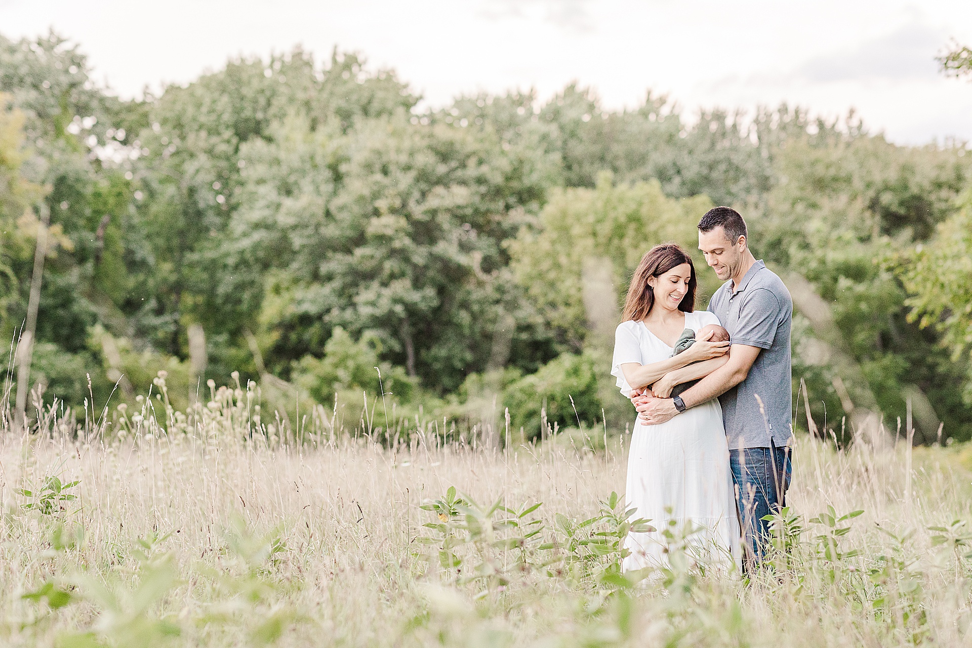 Parents hold newborn in field of tall grass during outdoor newborn photo session with Sara Sniderman Photography at Heard Farm, Wayland Massachusetts