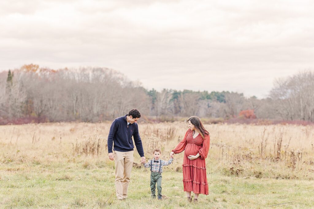 Family holds hands and walks during photo session with Sara Sniderman Photography at Cow Common, Wayland Massachusetts