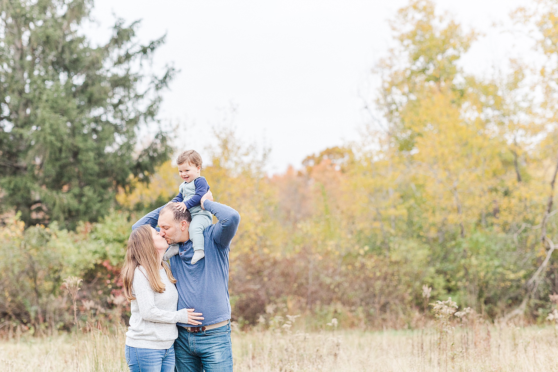dad holds son on shoulders and kisses wife during photo session with Sara Sniderman Photography at Cow Common, Wayland Massachusetts