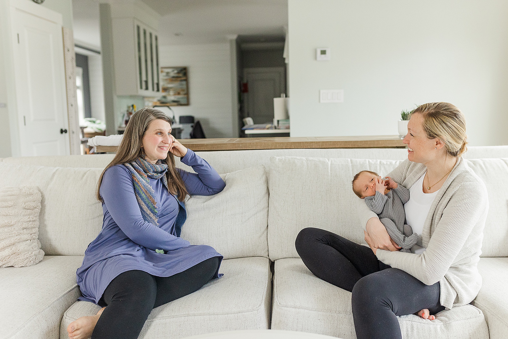 mom holding baby sits on couch with doula during branding photo session with Sara Sniderman Photography for Burgeoning Bud Postpartum doula and Pediatric Sleep Consultant