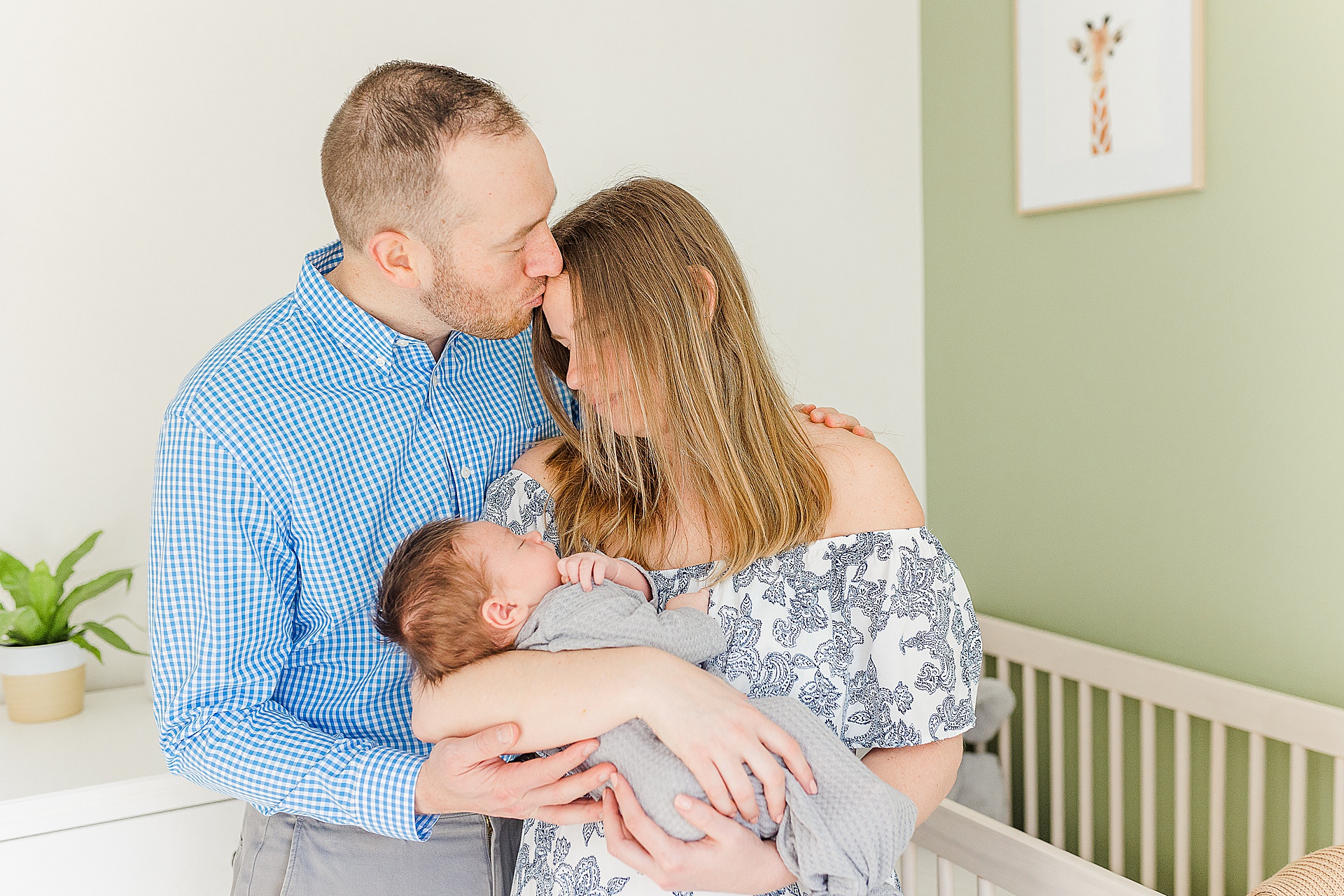man kisses wife head while holding baby in nursery during in home newborn photo session with Sara Sniderman Photography 
