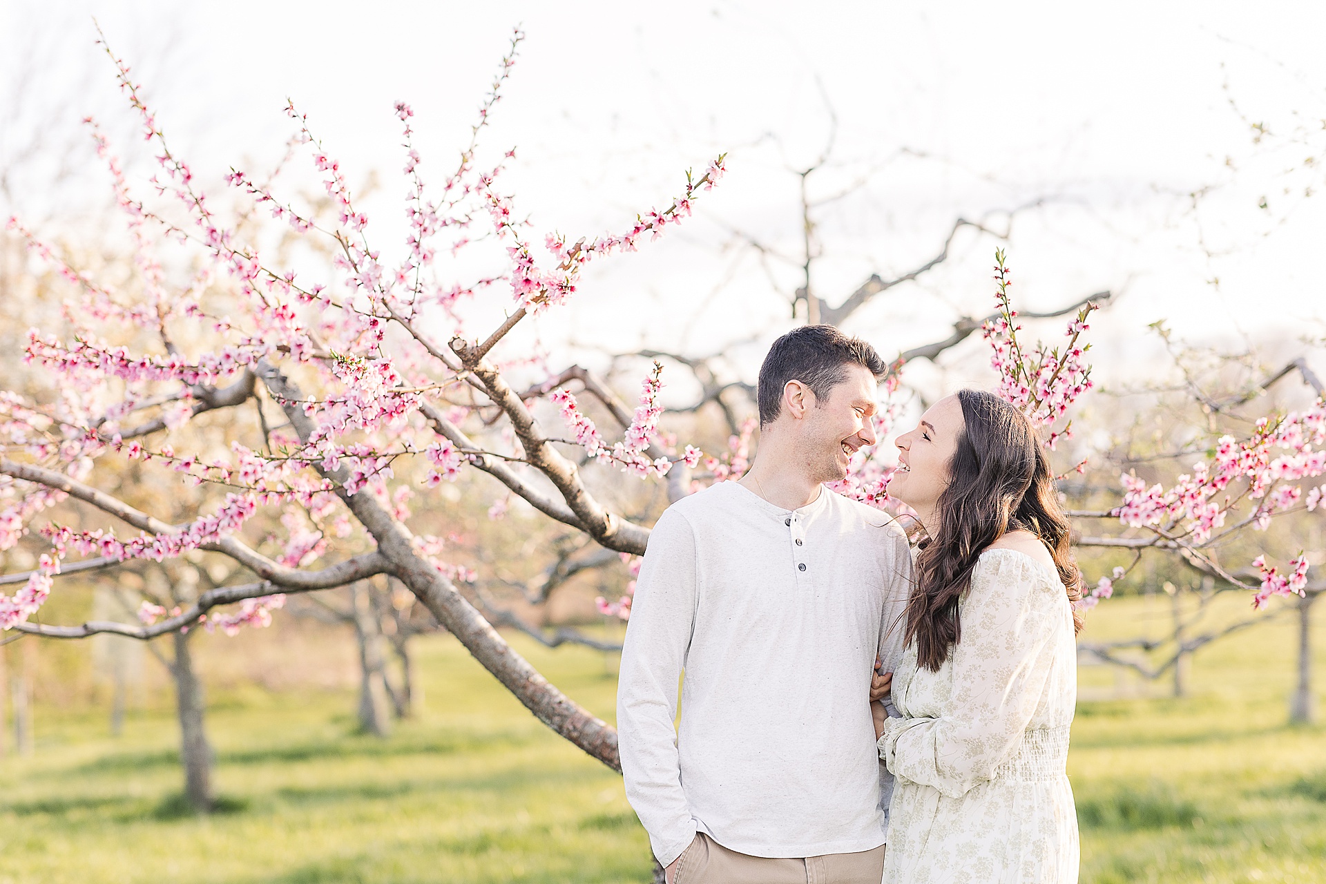couple smiles at each other during apple blossom family photo session at Heard Farm in Wayland Massachusetts with Sara Sniderman Photography