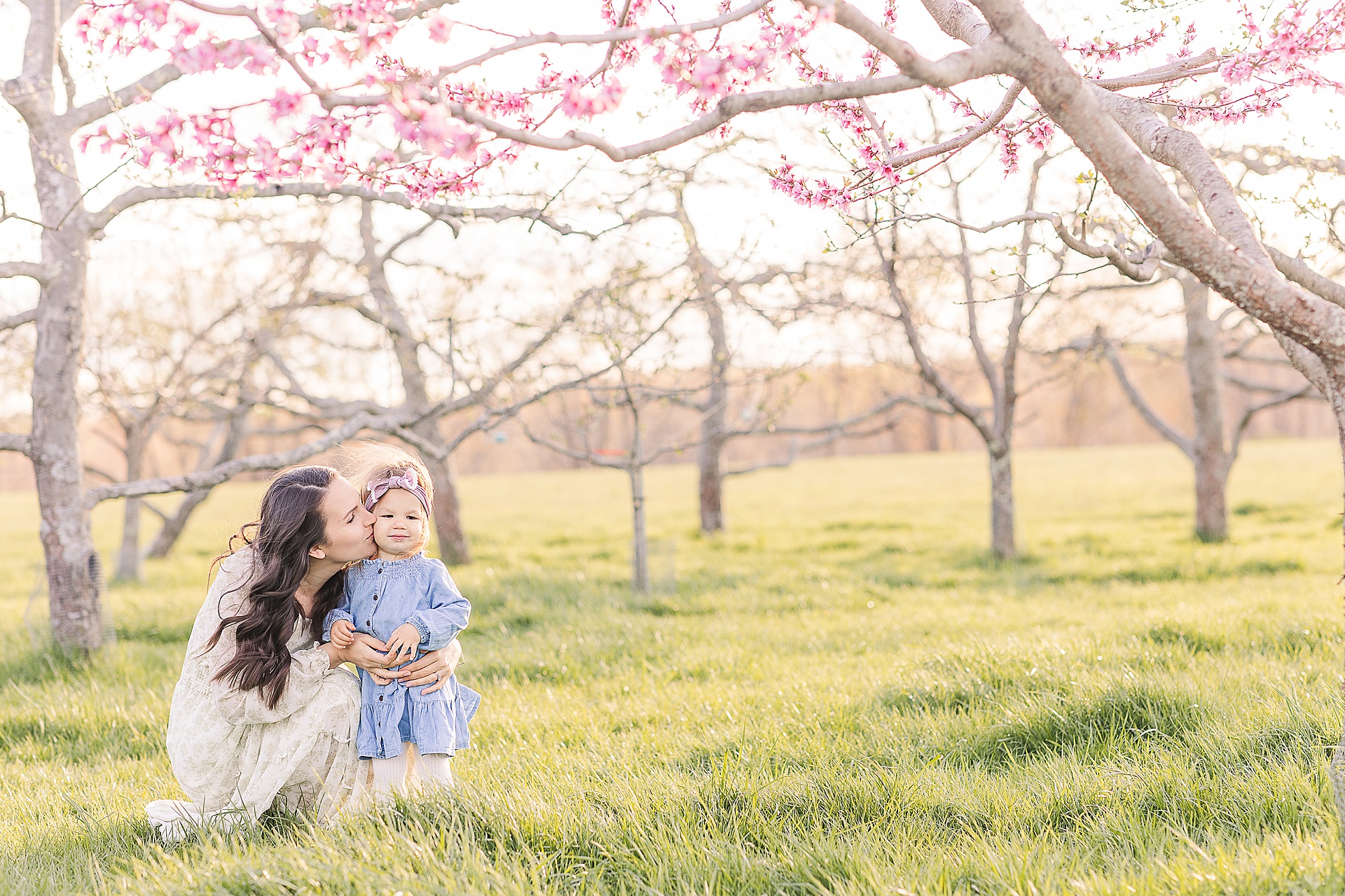 mom kisses daughter on the cheek during apple blossom family photo session at Heard Farm in Wayland Massachusetts with Sara Sniderman Photography
