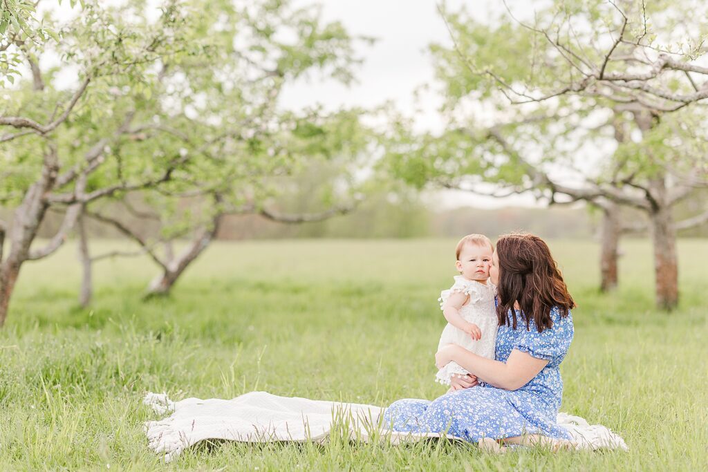 Mother sits on blanket with one year old daughter during first birthday family photo session with Sara Sniderman Photography at Heard Farm in Wayland Massachusetts