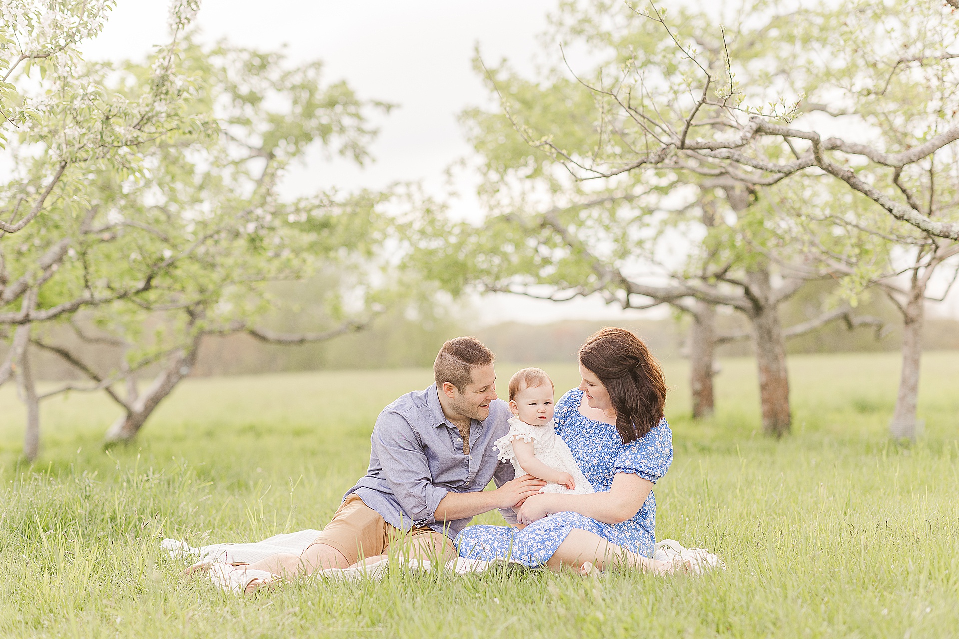 parents sit on blanket with baby during first birthday family photo session with Sara Sniderman Photography at Heard Farm in Wayland Massachusetts